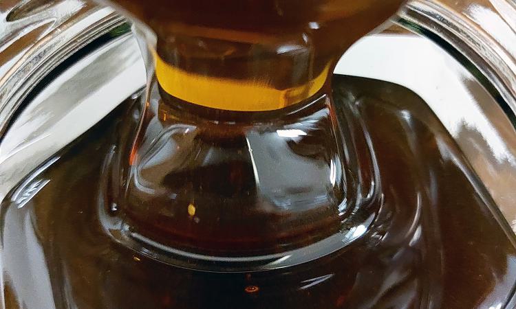 Nahaufnahme von goldbraunem Honig, der in ein Glas fließt