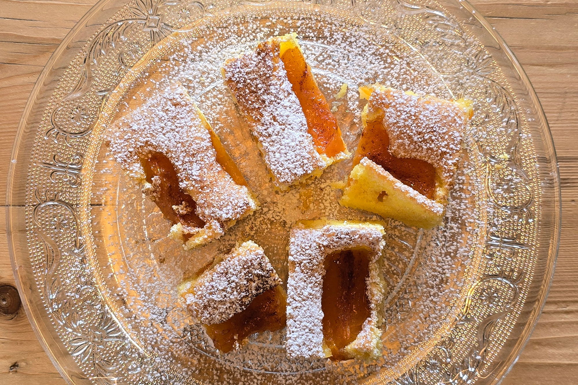 Fünf Stücke Marillenkuchen mit Puderzucker bestäubt, auf einem verzierten Glasteller
